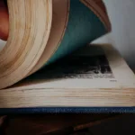 a person is holding an open book with a blue cover